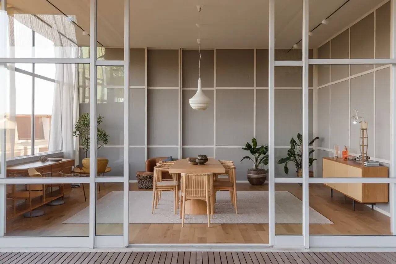Un intérieur moderne avec une salle à manger minimaliste comprenant une table en bois, des chaises assorties et des plantes décoratives, visible à travers