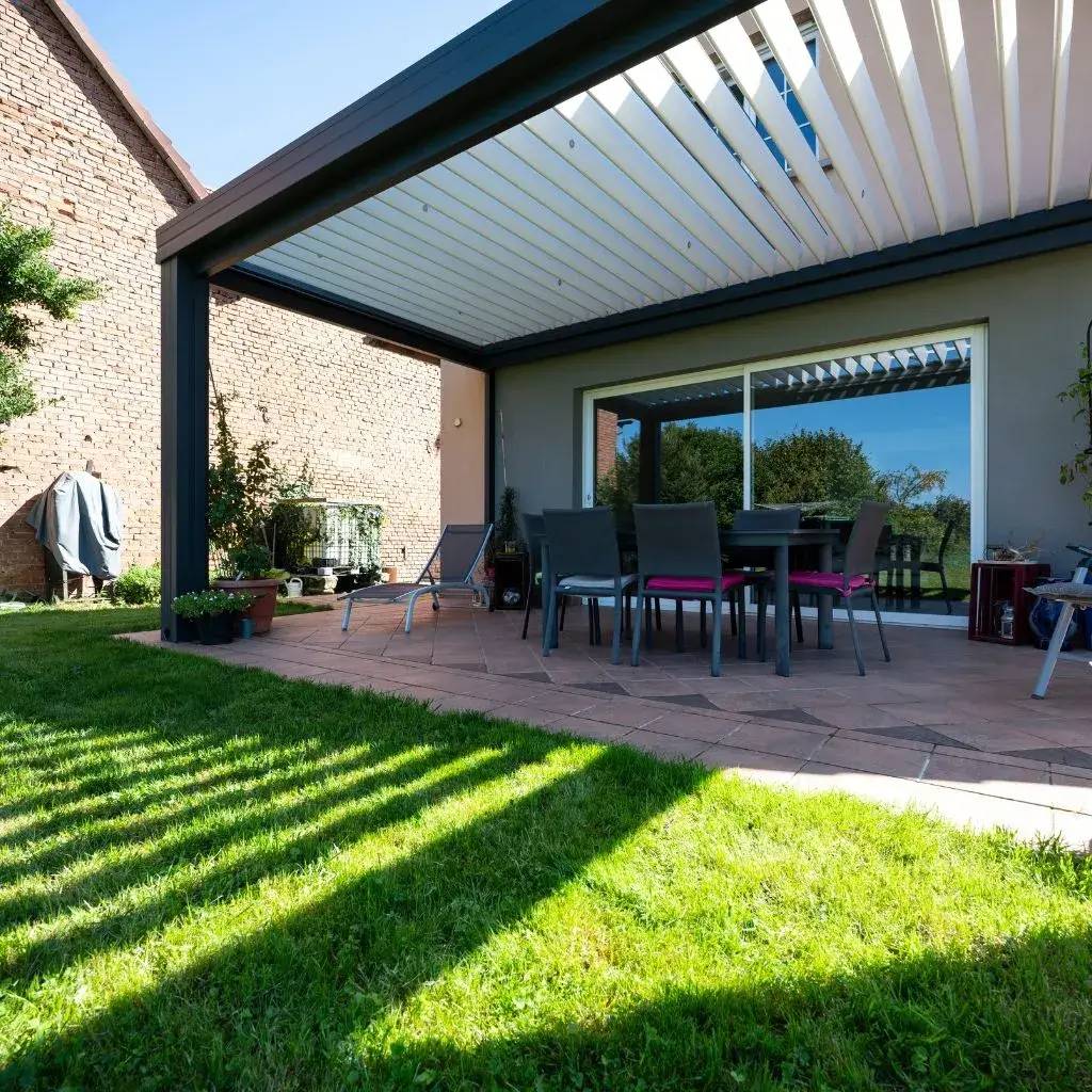 Cette image montre une terrasse moderne avec pergola, entourée de verdure, équipée de meubles d'extérieur pour les repas et la détente.