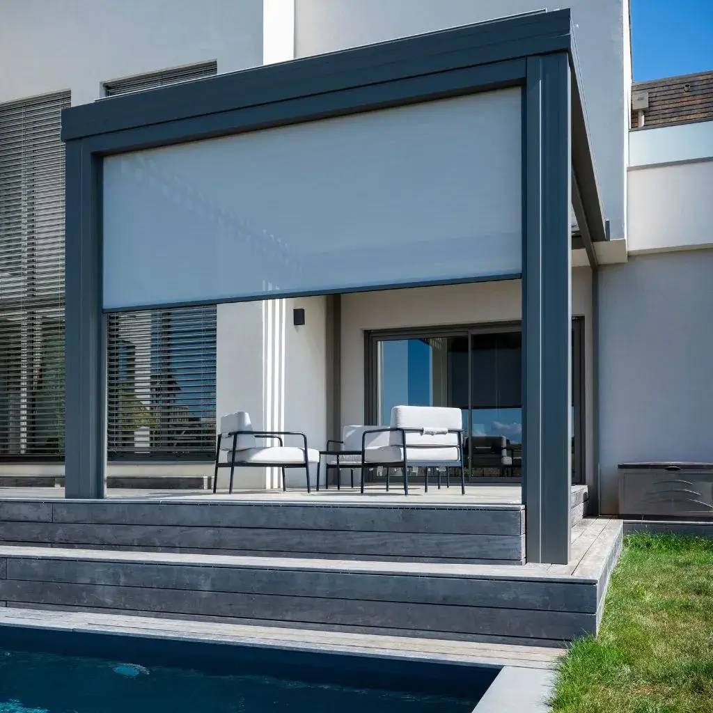 Une terrasse moderne avec un auvent rétractable gris, des fauteuils élégants et une piscine en contrebas, idéal pour la détente.