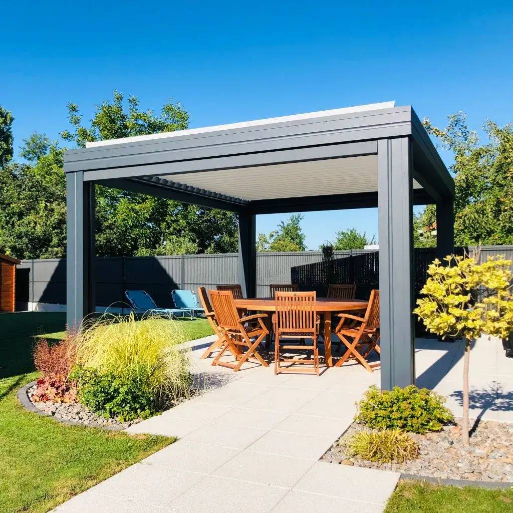 Une élégante pergola en métal abrite un salon de jardin en bois sur une terrasse entourée de verdure.