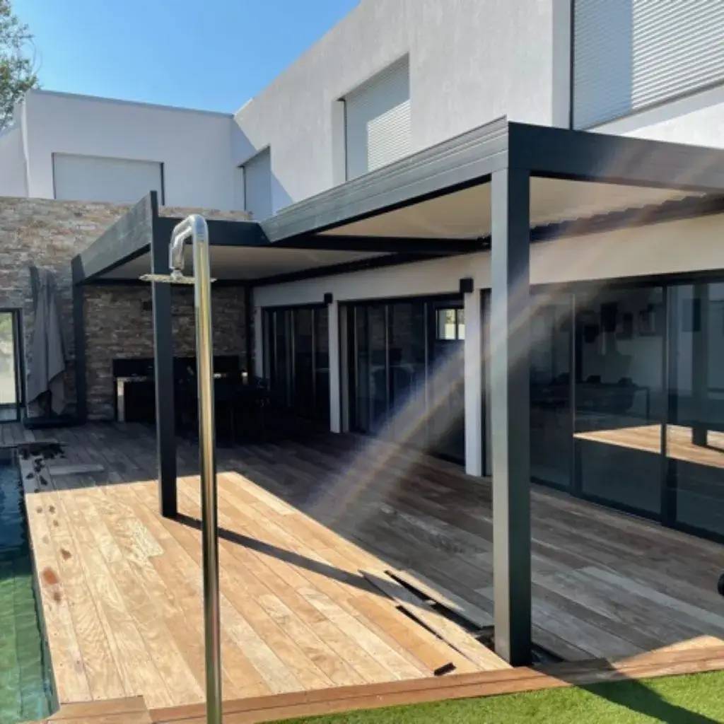 Terrasse moderne avec pergola en métal, plancher en bois et grandes baies vitrées près d'une piscine.