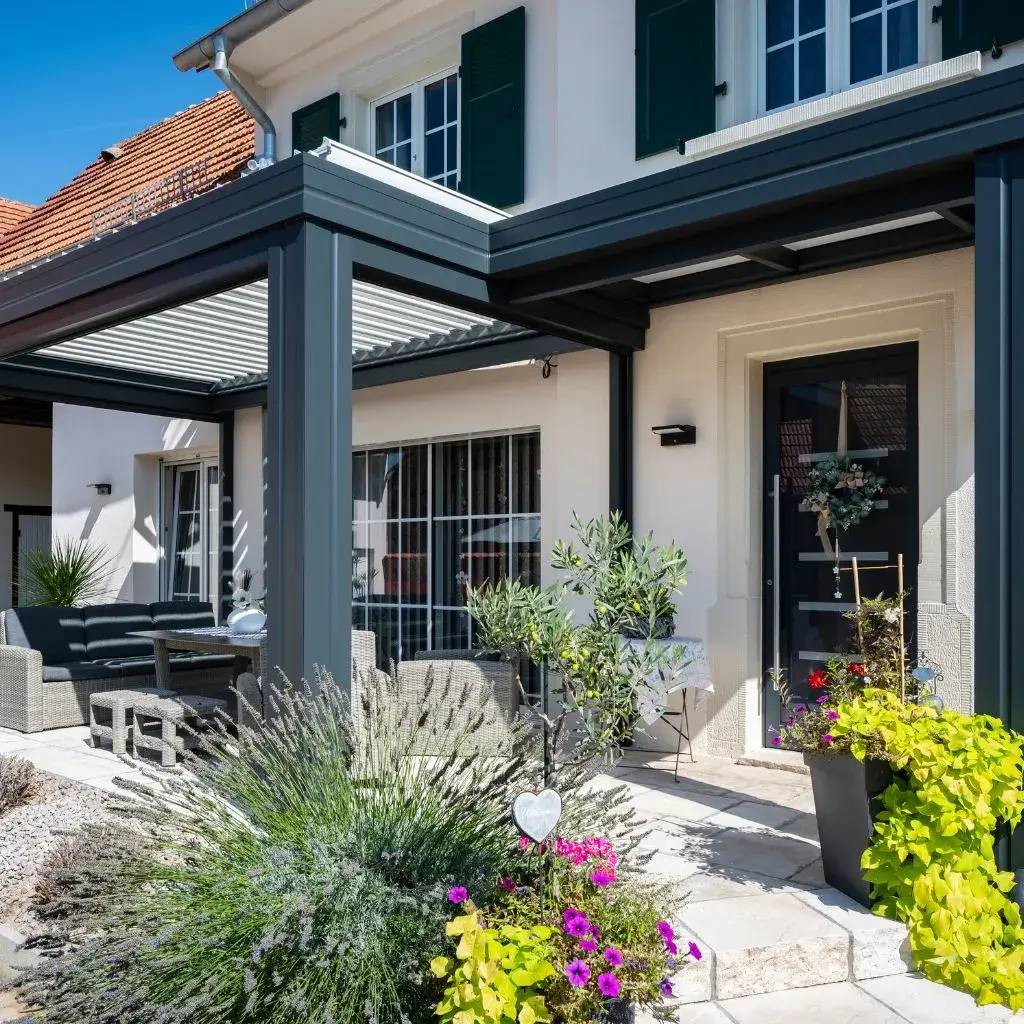 Une élégante terrasse moderne agrémentée de mobilier confortable et entourée de plantes fleuries en pots, le tout sous un ciel bleu éclatant