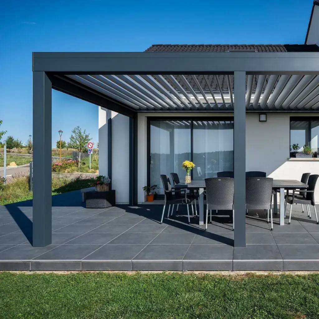 Une terrasse moderne avec une pergola bioclimatique et un ensemble de mobilier d'extérieur sous un ciel bleu.
