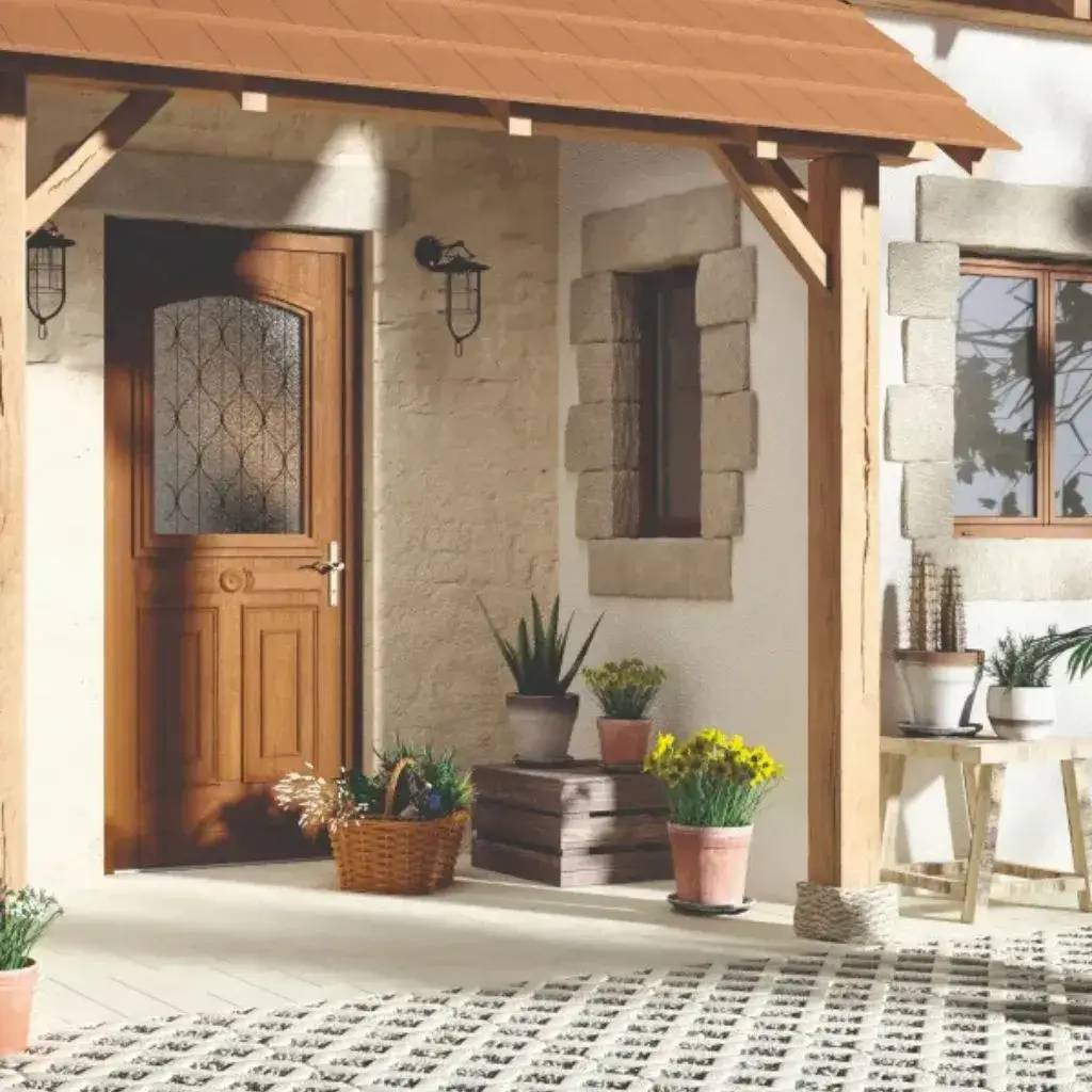 Une entrée de maison chaleureuse avec une porte en bois, entourée de pots de fleurs et de plantes sur un sol pavé.