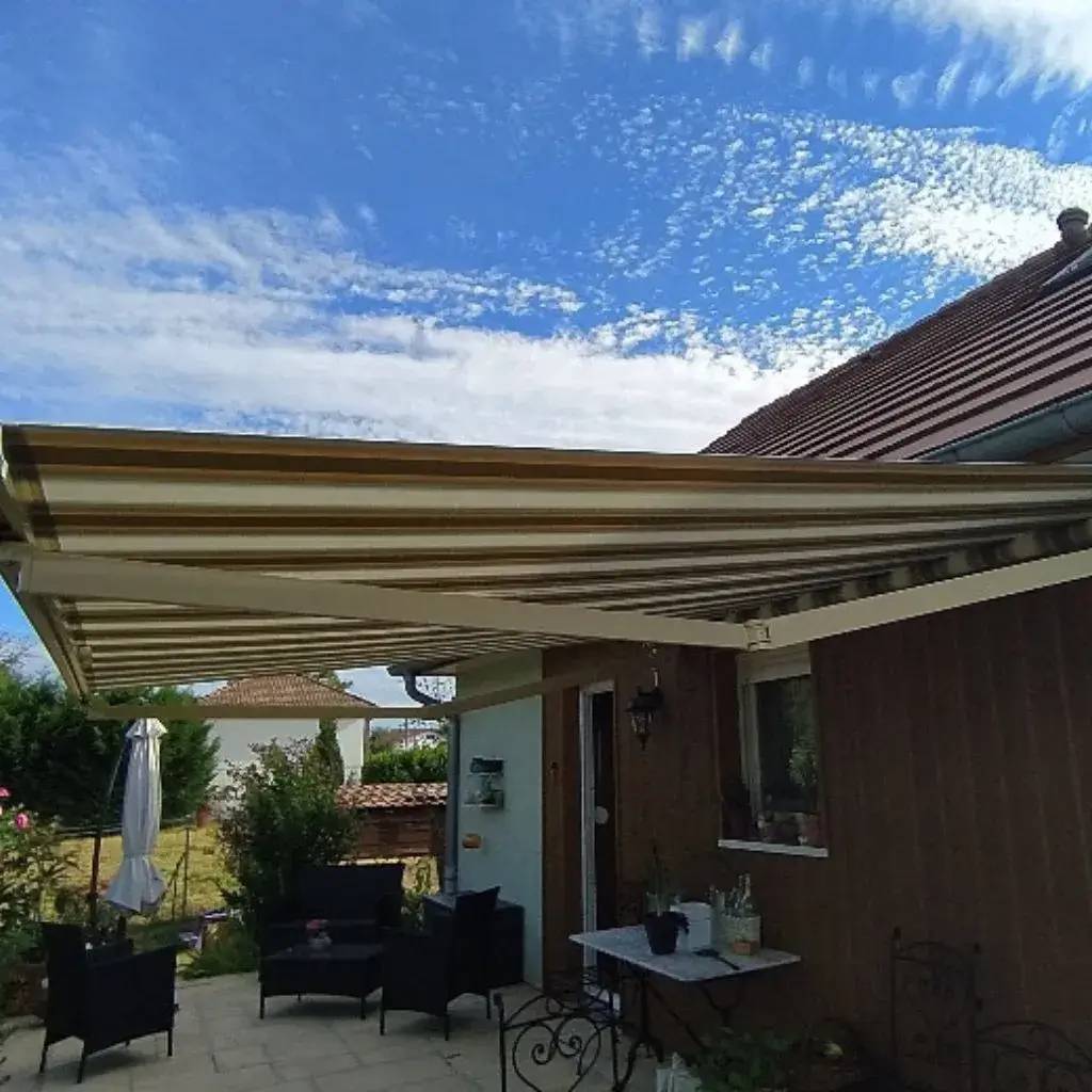 Un store banne déployé couvre une terrasse avec du mobilier de jardin sous un ciel partiellement nuageux.
