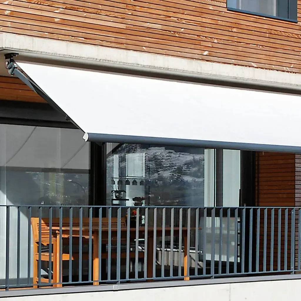 Un store blanc moderne recouvre partiellement une terrasse en bois, offrant de l'ombre à une table et des chaises en bois.