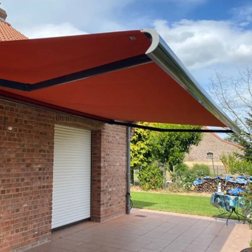 Un store banne orange est déployé au-dessus d'une terrasse en briques, offrant de l'ombre à l'extérieur de la maison.