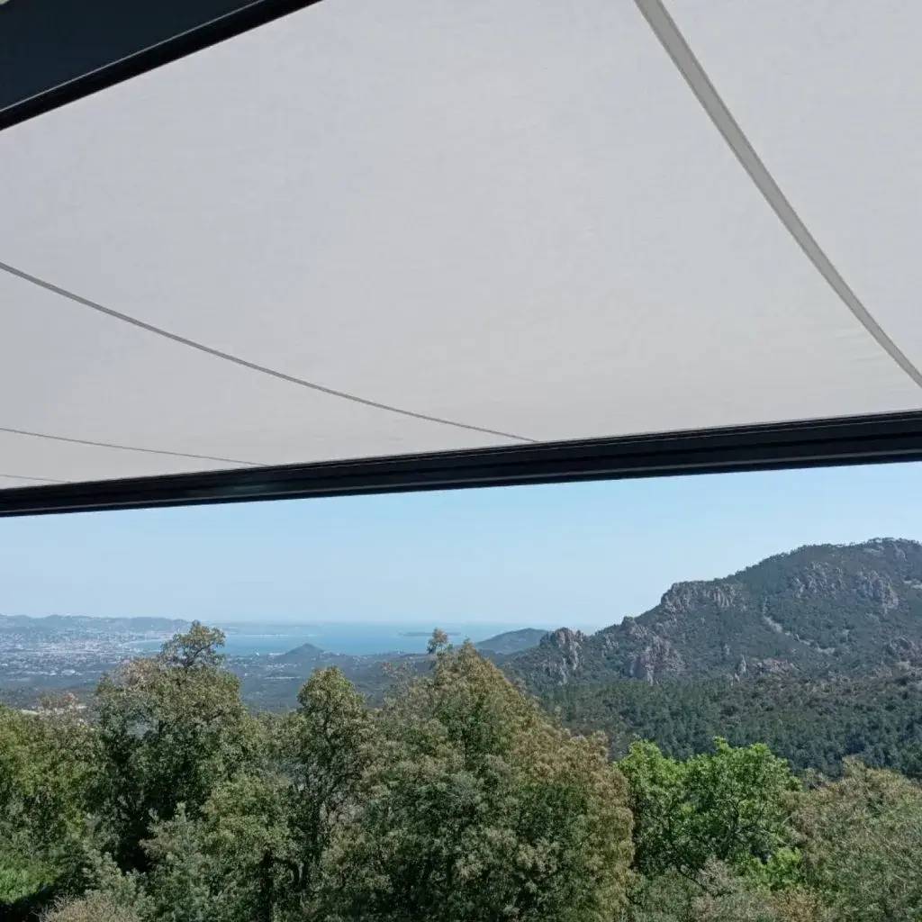 Vue panoramique sur des montagnes verdoyantes et la mer au loin, encadrée par un auvent moderne.