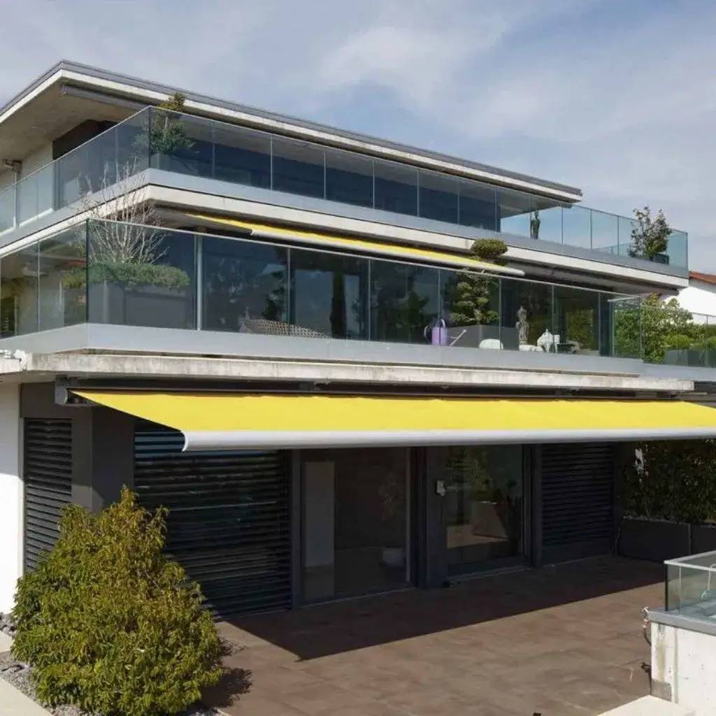 Une maison moderne à plusieurs niveaux avec de grandes terrasses en verre et un auvent jaune.