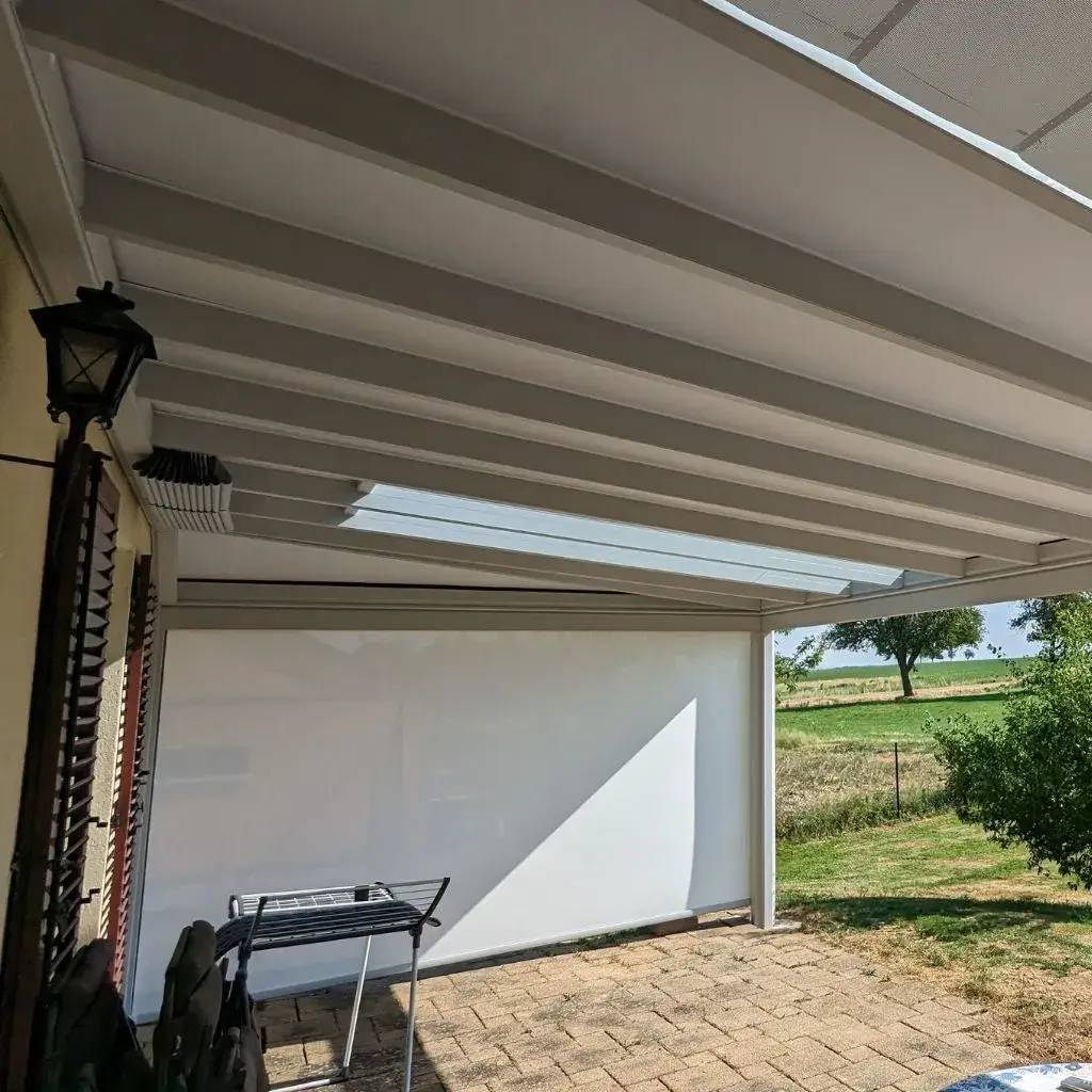 Un patio extérieur couvert par une pergola moderne blanche offre une vue dégagée sur un jardin verdoyant.