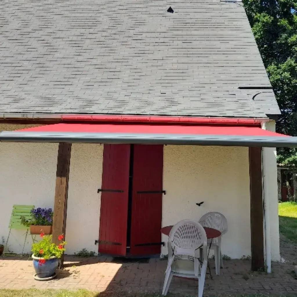 Un abri de jardin avec une porte rouge, équipé d'un auvent assorti et entouré de chaises et de pots de fleurs.