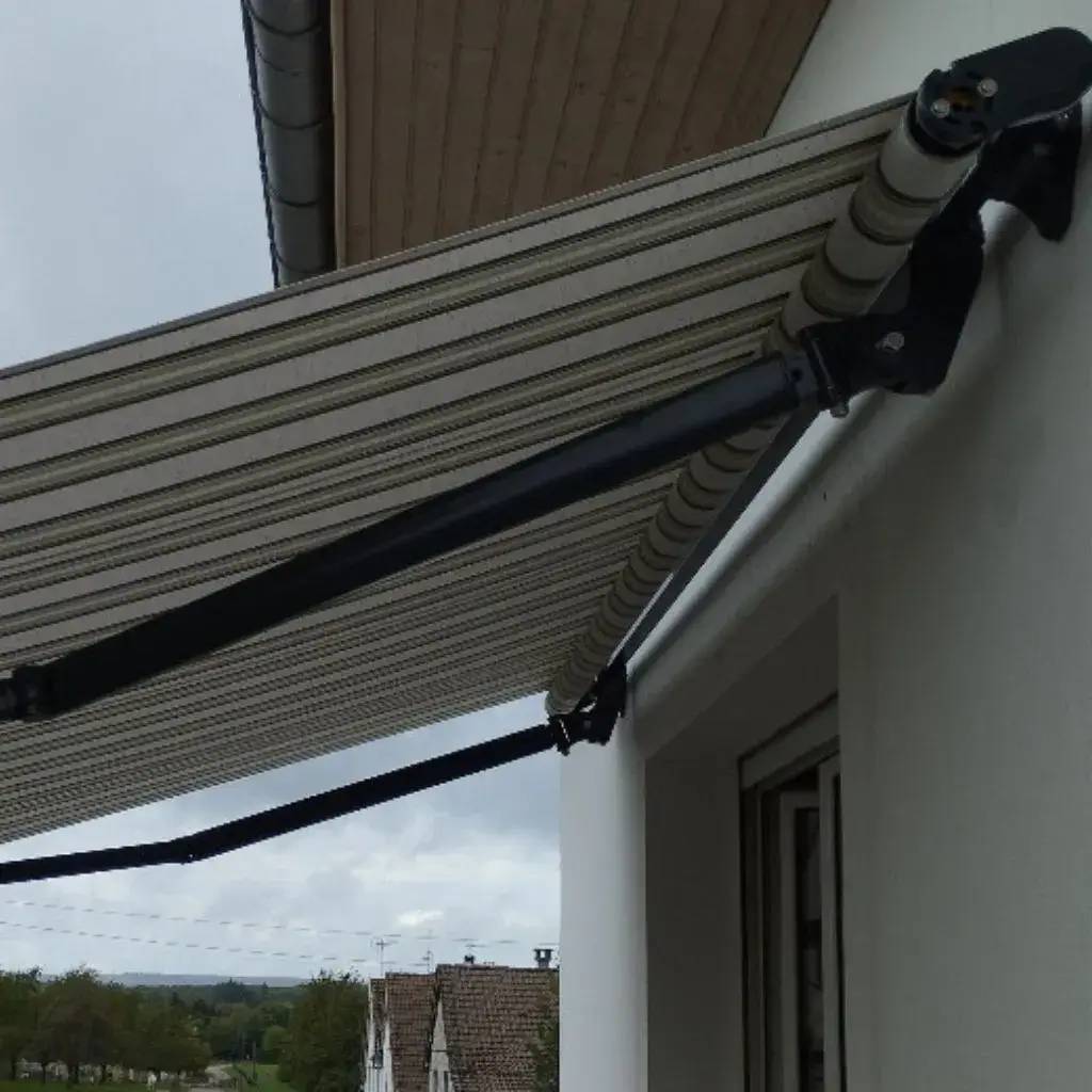 Un store banne rayé est déployé sur une terrasse, offrant de l'ombre par temps couvert.