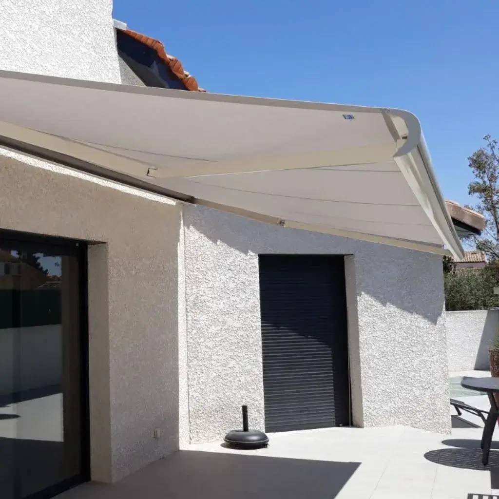 Une terrasse moderne avec un store banne beige évasé sur une façade de maison en crépi blanc.
