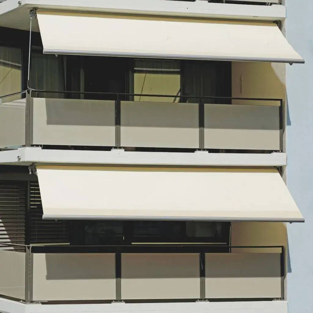 Façade d'un bâtiment moderne avec des balcons équipés de stores beige déployés.