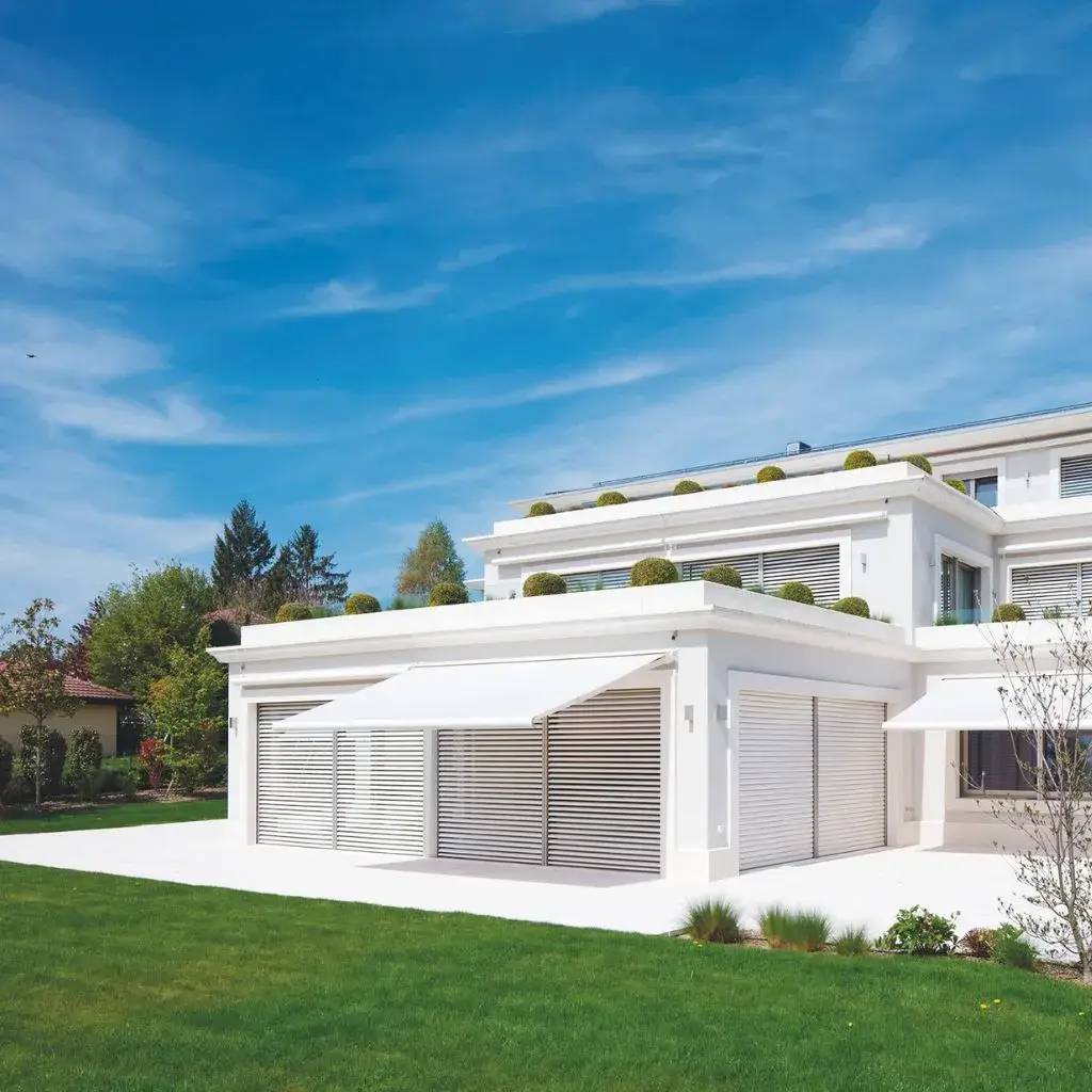 Une maison moderne et lumineuse avec une façade blanche et un jardin bien entretenu sous un ciel bleu.