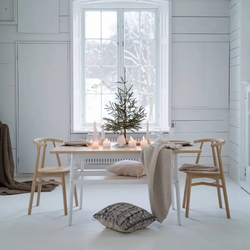 Une salle à manger minimaliste et lumineuse avec une table décorée de bougies et d'un petit sapin, entourée de chaises en