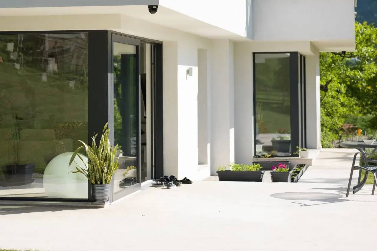 Terrasse moderne et épurée avec de grandes fenêtres et des plantes en pot, offrant une vue lumineuse sur l'extérieur.