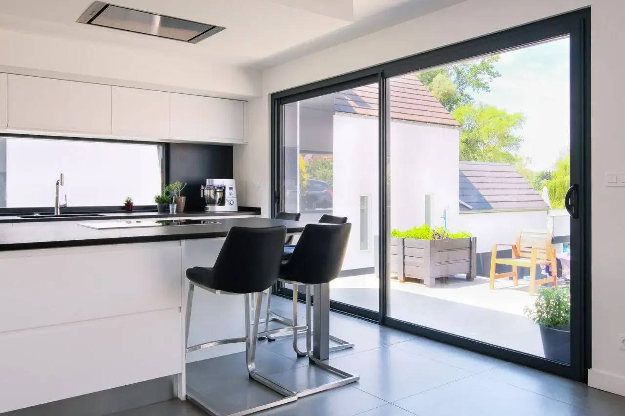 Cuisine moderne et lumineuse avec grandes baies vitrées donnant sur une terrasse.