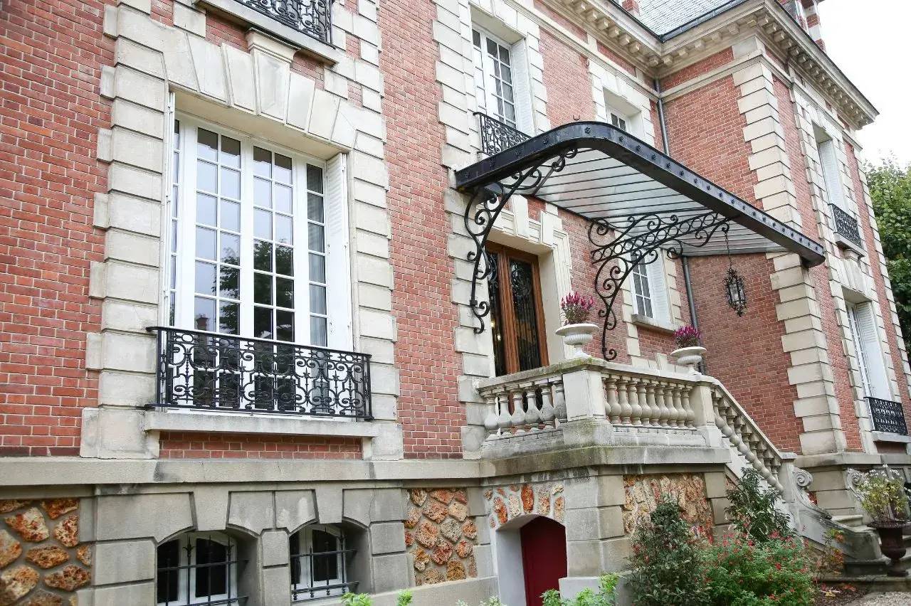 Façade d'un bâtiment en briques rouges avec des balustrades et une marquise métallique ornée.