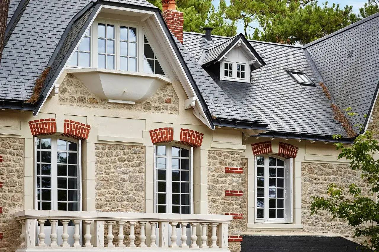 Une belle maison en pierre avec un toit en ardoise, des fenêtres à volets blancs et des détails en briques rouges.