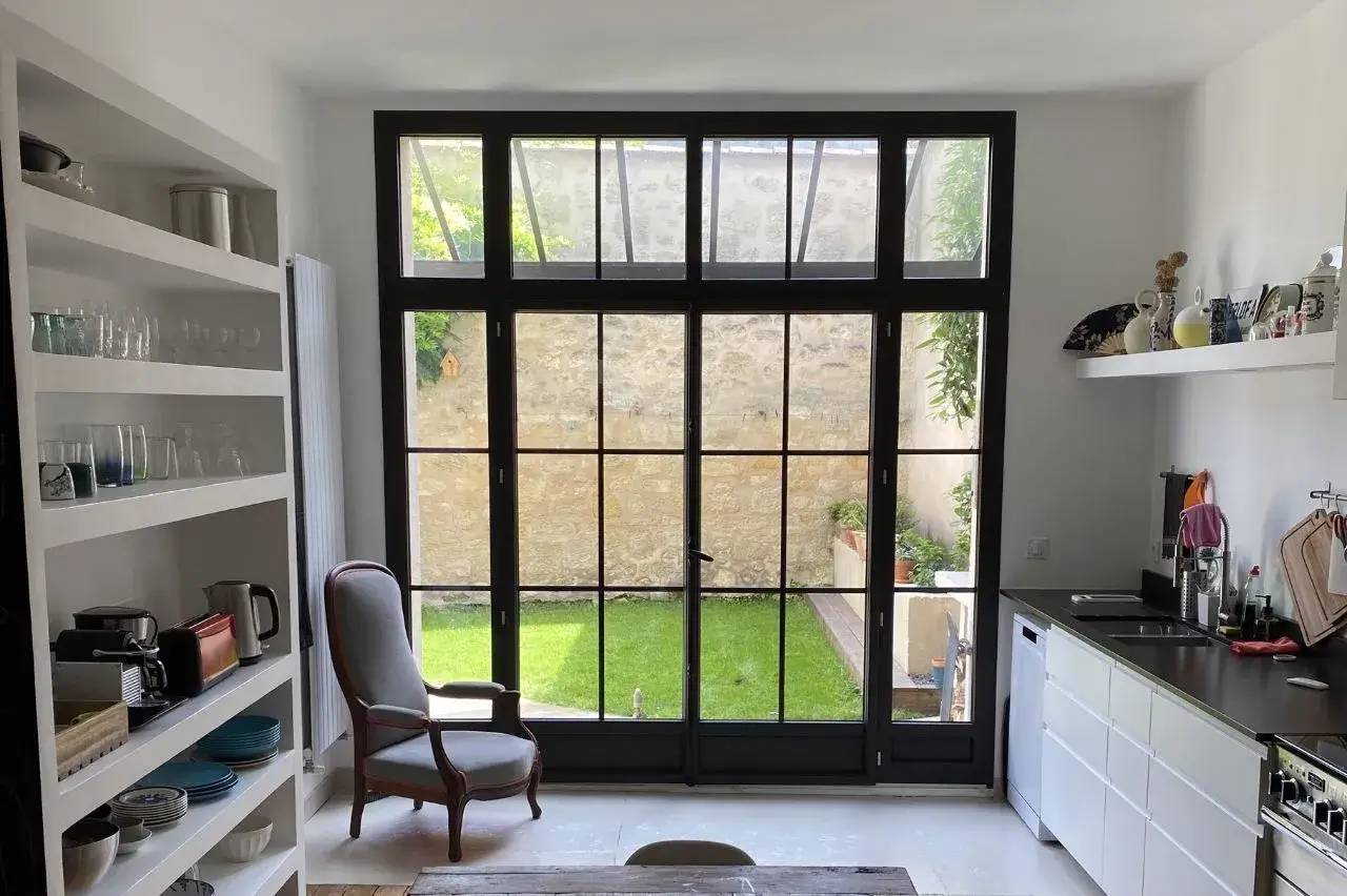 Cuisine lumineuse avec verrière donnant sur un jardin, équipée de rangements intégrés et d’une décoration épurée.