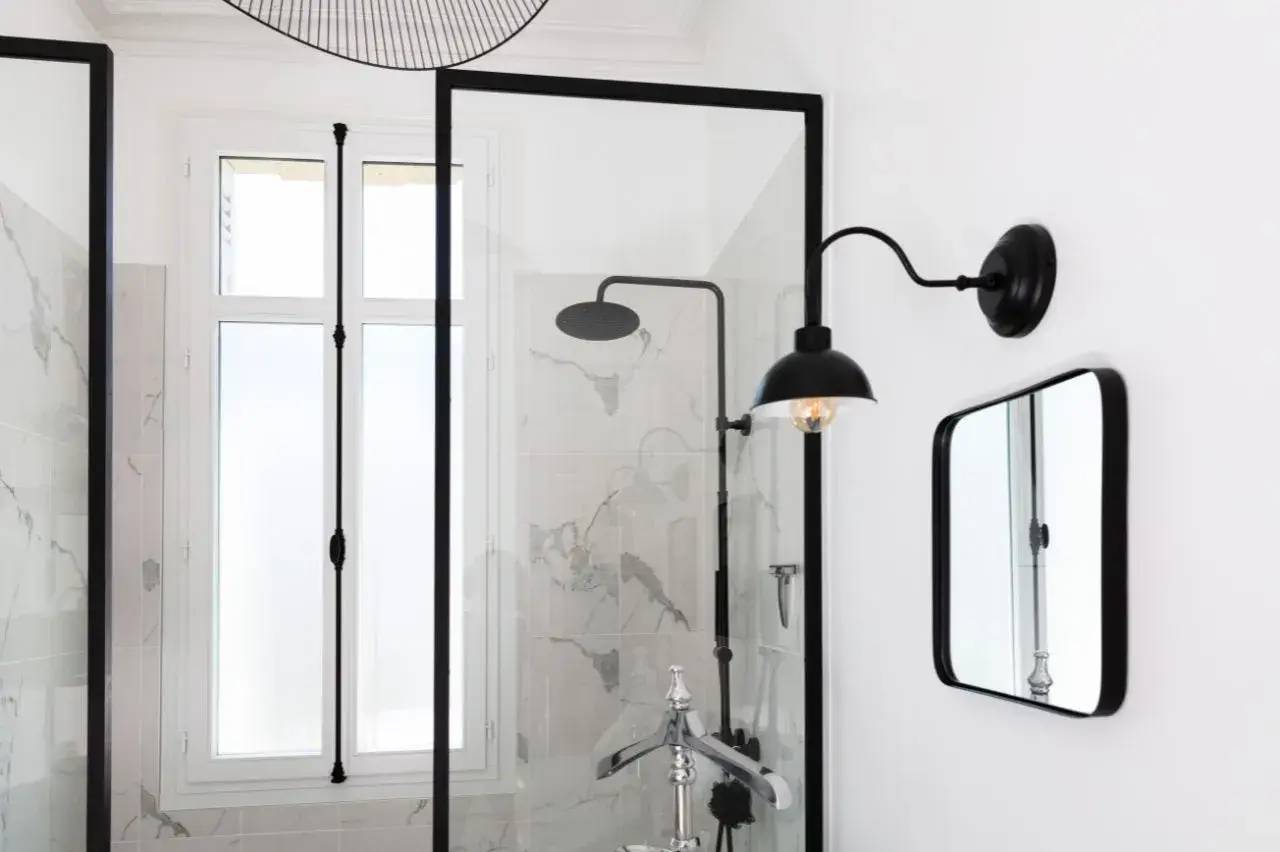 Salle de bain élégante avec douche à l'italienne en verre et applique murale noire au design moderne.