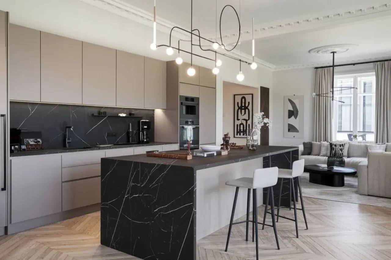 Une cuisine moderne et élégante avec un îlot central en marbre noir et un éclairage design, ouverte sur un salon lumineux.
