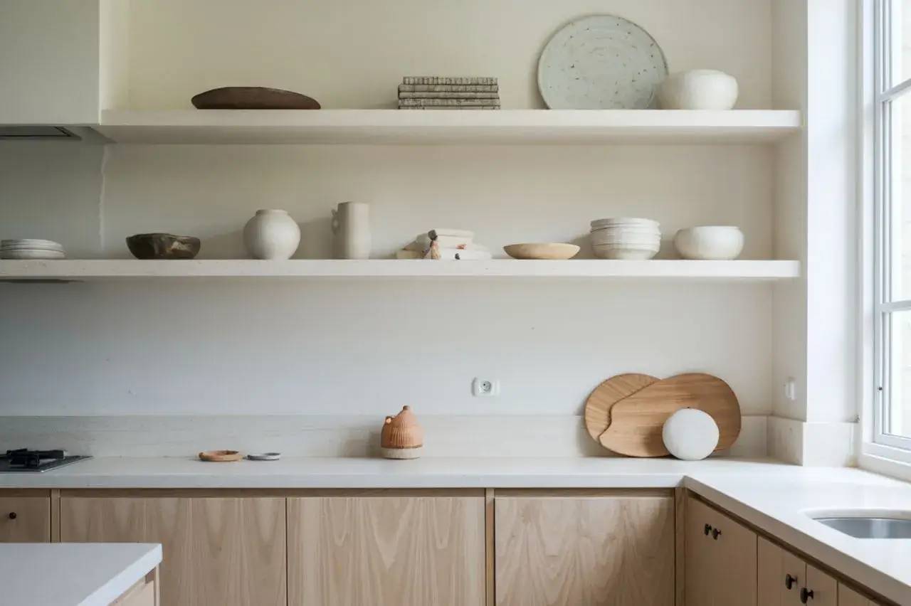 Cuisine minimaliste avec des étagères ouvertes exposant de la vaisselle en céramique et en bois sur un plan de travail blanc.