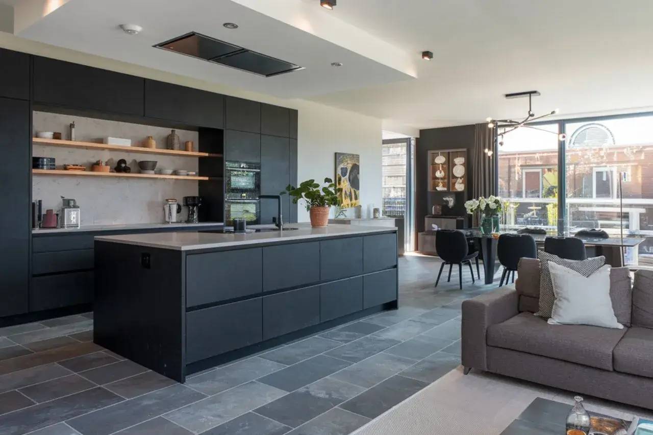 Cuisine moderne et élégante avec îlot central noir, espaces de rangement ouverts et coin repas intégré dans un environnement lumineux.