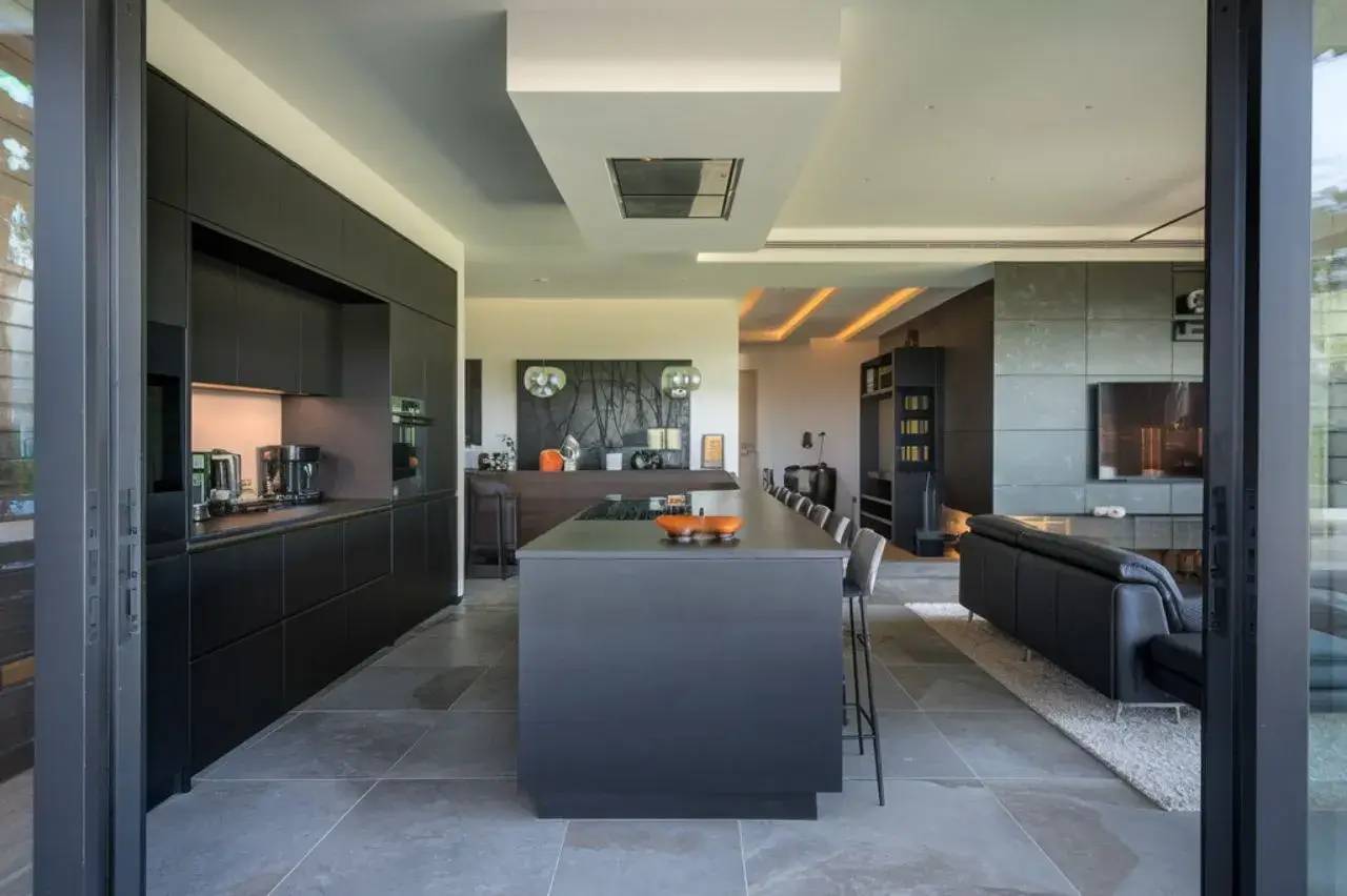 Vue d'une cuisine moderne et spacieuse avec des armoires noires, un îlot central et un salon attenant.