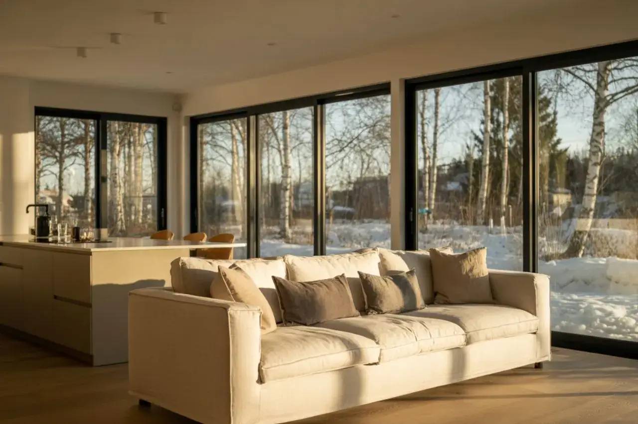 Un salon moderne et lumineux avec un grand canapé beige et de larges baies vitrées offrant une vue sur un paysage enneigé.