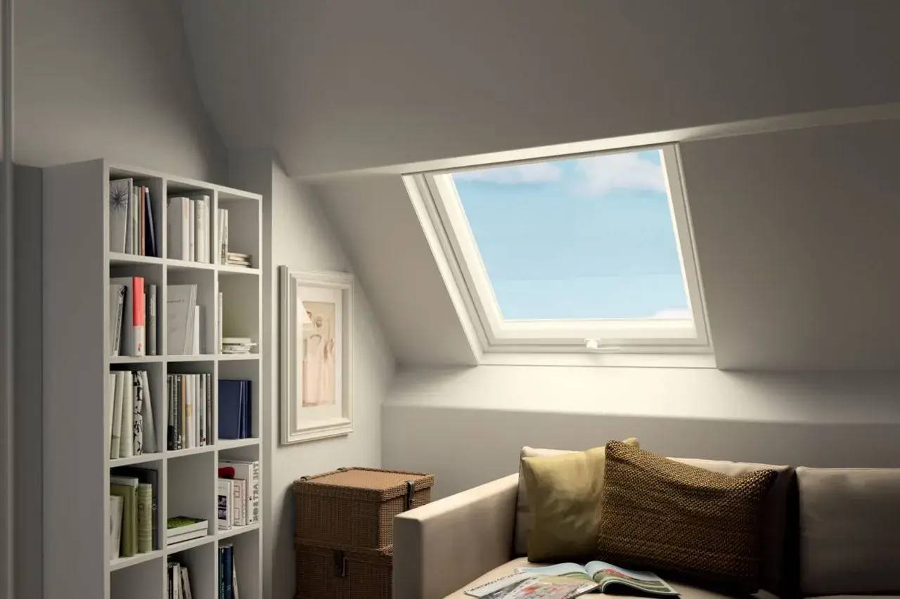 Une pièce lumineuse sous les combles, aménagée avec une grande fenêtre de toit, une bibliothèque et un canapé confortable.