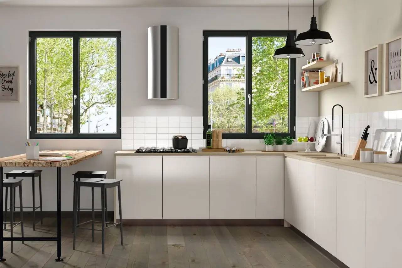 Une cuisine moderne et lumineuse avec de grandes fenêtres, des armoires blanches, et un îlot central en bois.