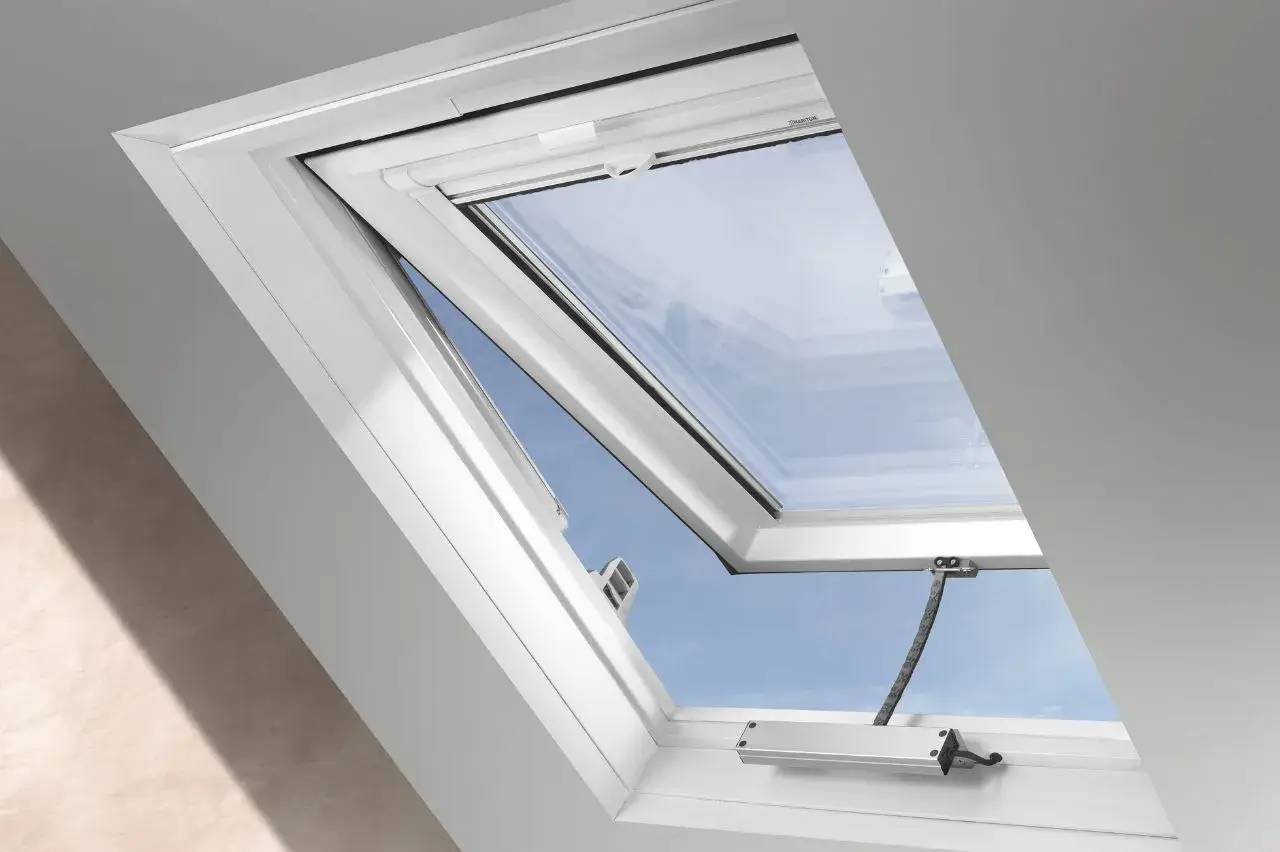 Une fenêtre de toit inclinée ouverte, laissant entrer la lumière naturelle sous un ciel bleu clair.