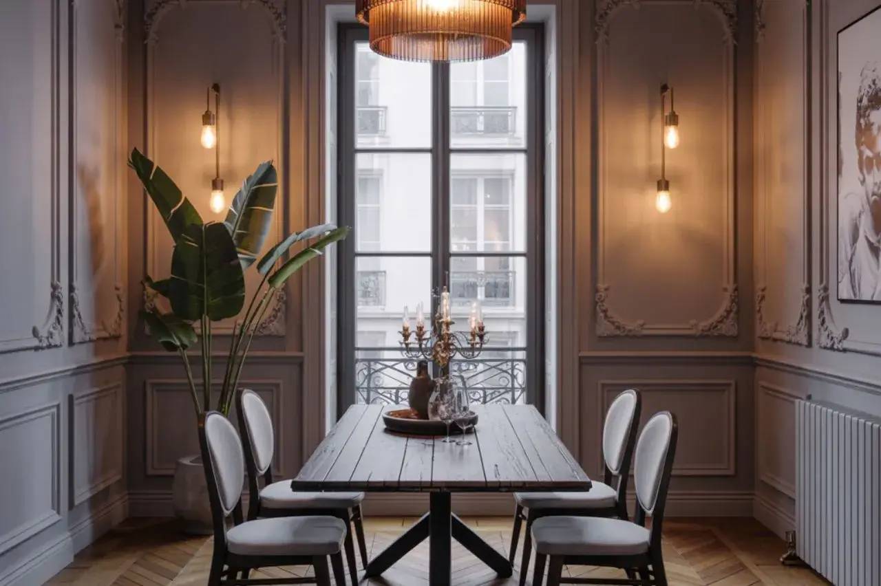 Une salle à manger élégante et classique avec un mobilier en bois sombre, des moulures murales décoratives, un lustre et des suspensions