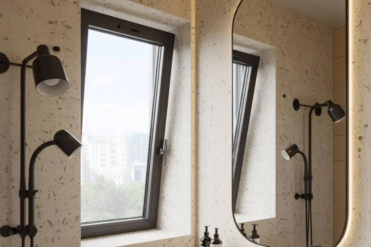 Une fenêtre inclinée laisse entrer la lumière naturelle dans une salle de bains moderne aux murs texturés, complétée par un miroir et une applique