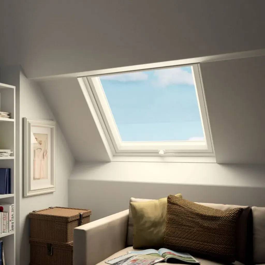 Cet espace lumineux de grenier est aménagé avec un canapé confortable, des coussins, une grande fenêtre de toit laissant entrer la lumière naturelle, et