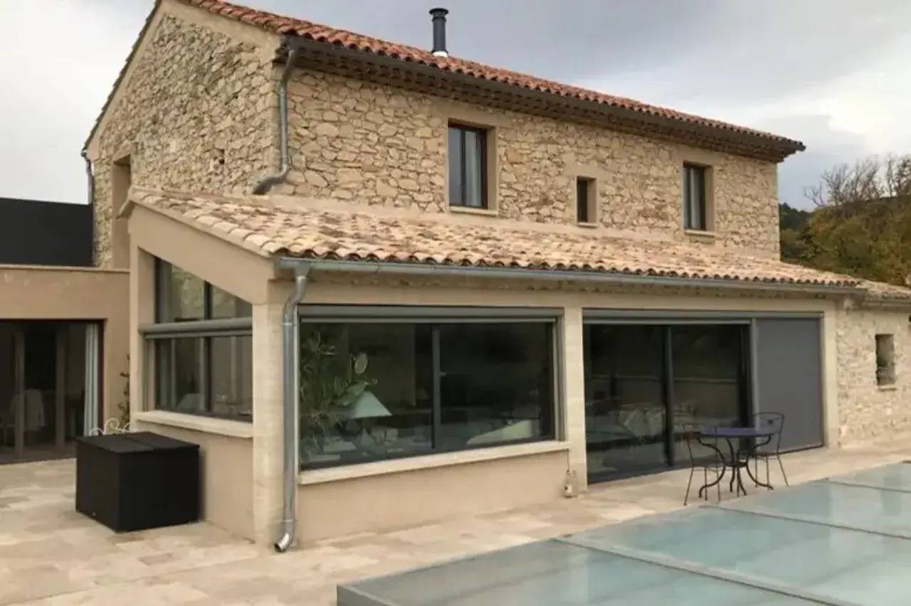 Cette image montre une maison en pierre avec de grandes baies vitrées et une terrasse en carrelage.