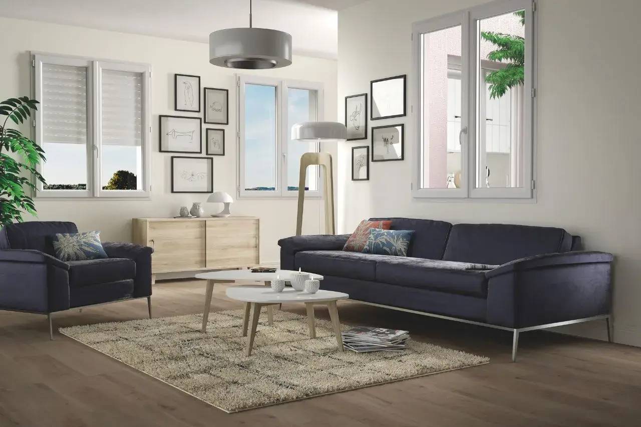 Un salon moderne et lumineux avec un canapé bleu, un tapis beige, des tables basses blanches et des cadres muraux artistiques.