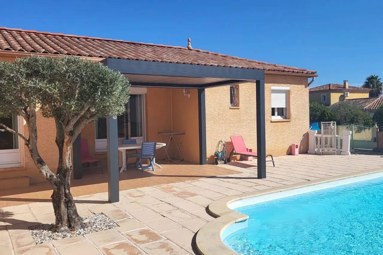 Une villa ensoleillée avec piscine, terrasse ombragée et un olivier sur un fond de ciel bleu.