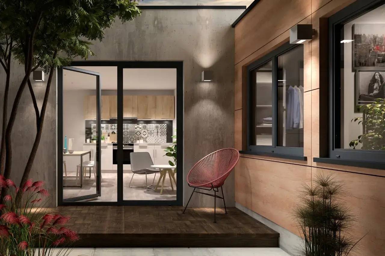Une terrasse moderne avec un fauteuil design s'ouvrant sur une cuisine lumineuse et élégante à travers des portes vitrées.