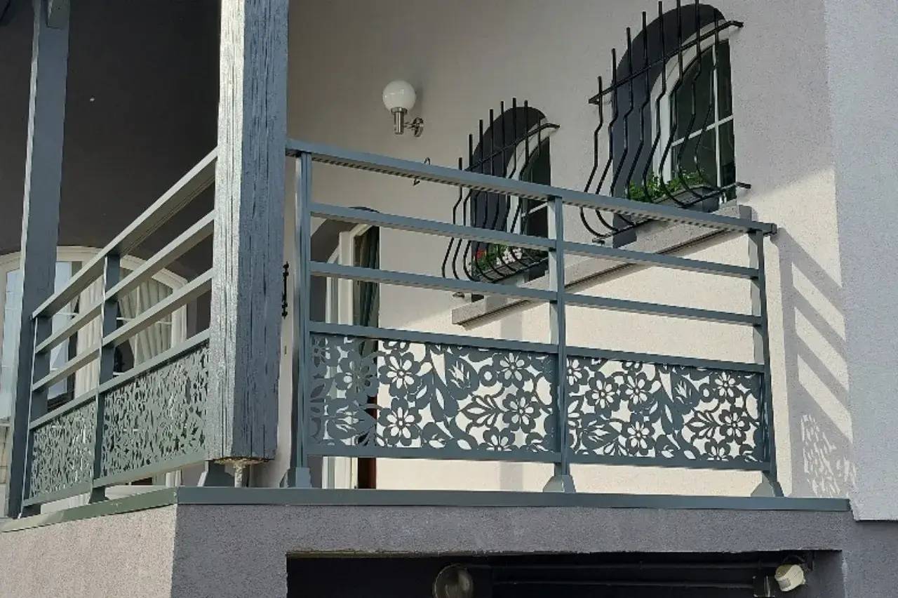 Un balcon moderne avec un garde-corps en métal décoratif à motifs floraux, accompagné de fenêtres équipées de grilles de sécurité élégantes.