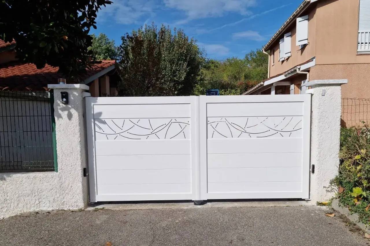 Portail blanc moderne avec motifs décoratifs en métal ajouré, installé devant une maison.