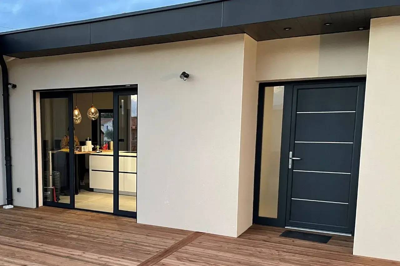 Une maison moderne avec une terrasse en bois, une grande baie vitrée et une porte d'entrée noire.
