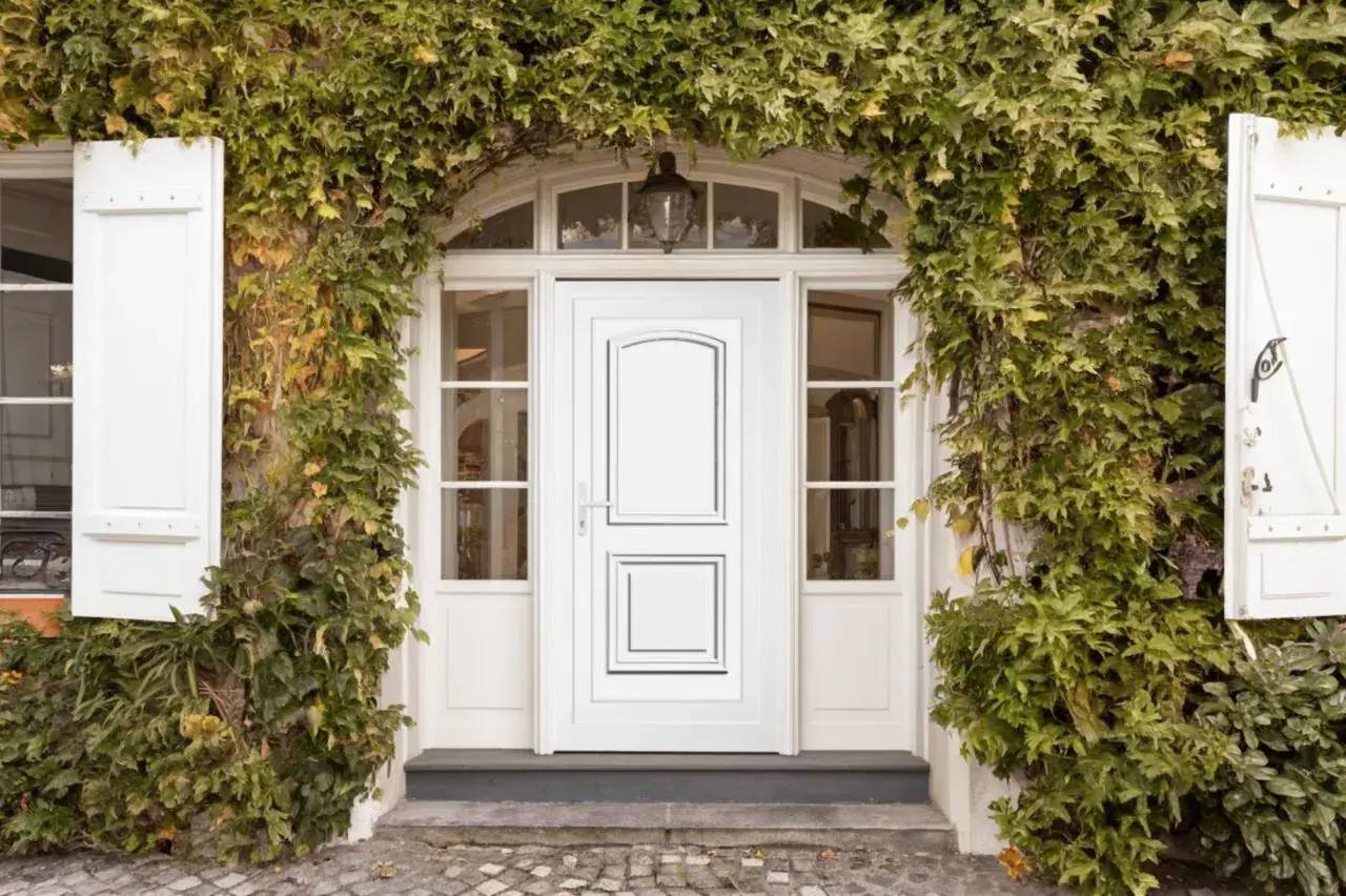 Façade de maison avec une porte blanche entourée de verdure luxuriante.