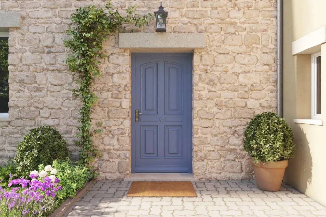 Porte bleue élégante encadrée de pierre, ornée de verdure et de fleurs colorées.