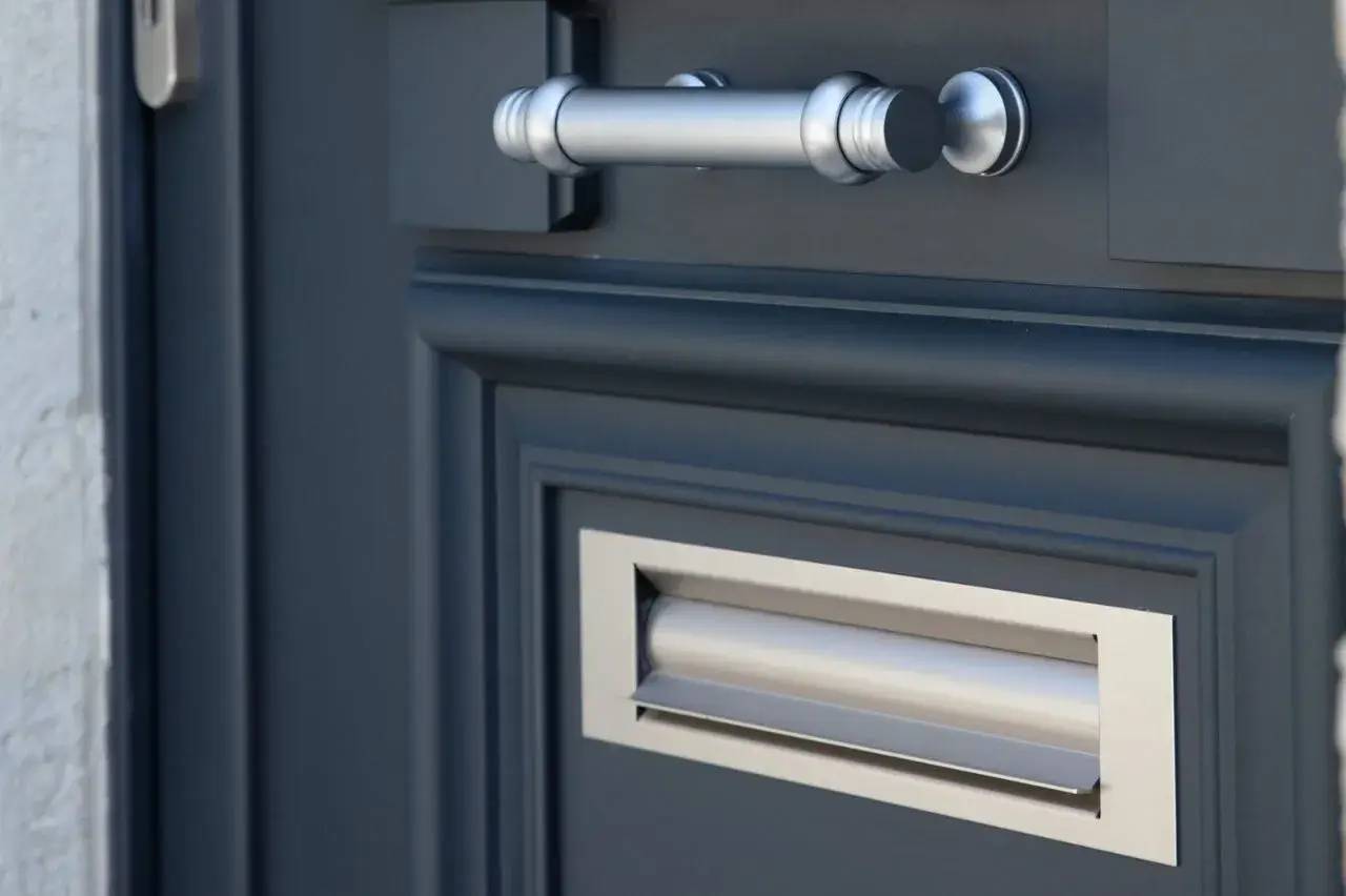 Gros plan sur une porte bleue avec une poignée métallique argentée et une fente pour lettres intégrée.