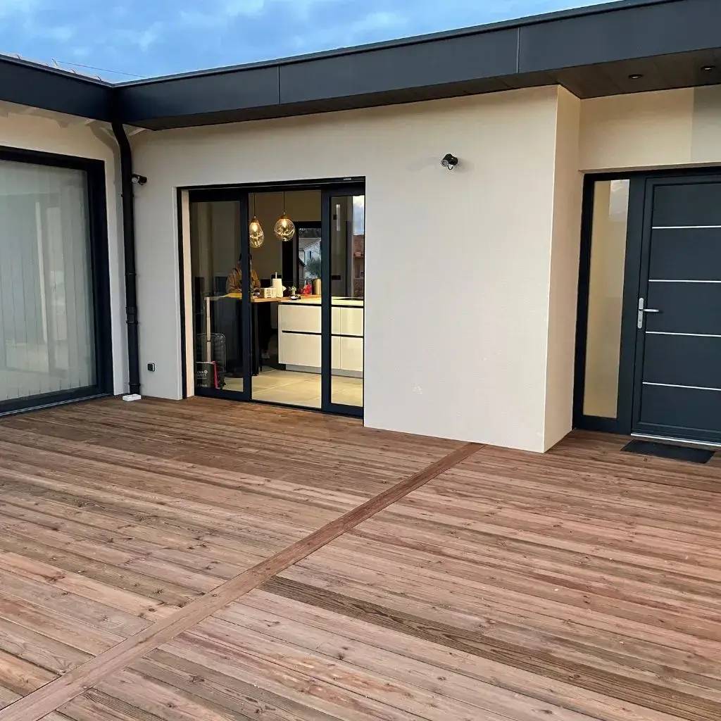 Une terrasse en bois spacieux donnant sur une maison moderne avec de grandes portes vitrées.