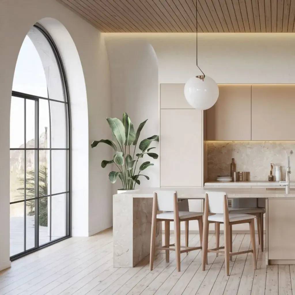 Une cuisine moderne et lumineuse avec des murs blancs, un îlot en marbre, des tabourets en bois clair, une grande fenêtre arqu