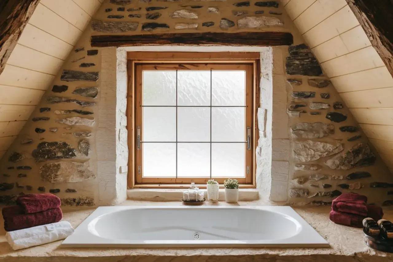 Une baignoire encastrée dans une salle de bain rustique avec murs en pierre et une fenêtre en bois.